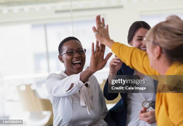 businesswomen high-fiving in office - office celebration stock pictures, royalty-free photos & images