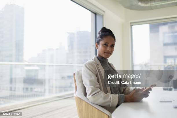 portrait confident businesswoman using smart phone in conference room - people watching at camera stock-fotos und bilder