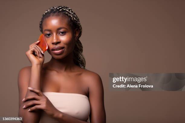 beautiful  young afro woman   using gua sha stone on beige background - cornrow braids stock-fotos und bilder