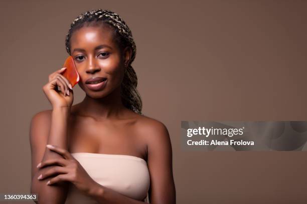 beautiful  young afro woman   using gua sha stone on beige background - beautiful south african women - fotografias e filmes do acervo
