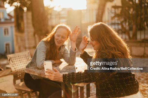 Two friends are using smartphone to have a video call with their family/friends outdoors at sunset