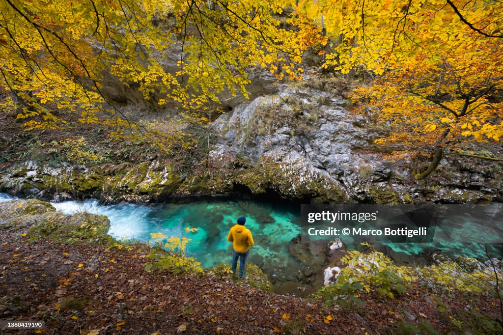 Man standing beside a turquoise river gorge in autumn