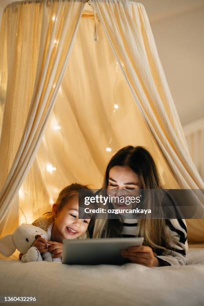 mother and daughter watching their digital tablet together lying in bed under the tent. - children on a tablet stockfoto's en -beelden