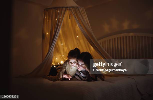 mother and daughter watching their digital tablet together lying in bed under the tent. - girl kissing screen stock pictures, royalty-free photos & images