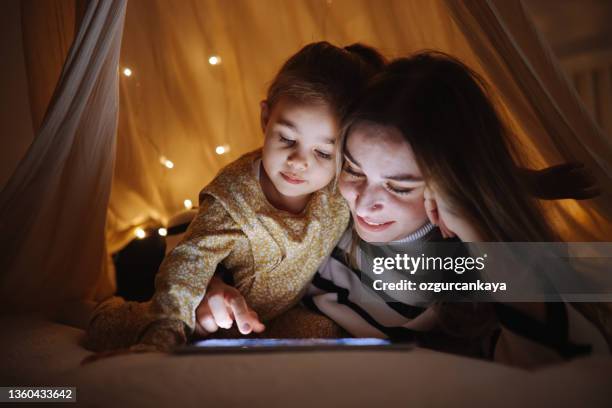 mother and daughter watching their digital tablet together lying in bed under the tent. - mother happy reading tablet stock pictures, royalty-free photos & images