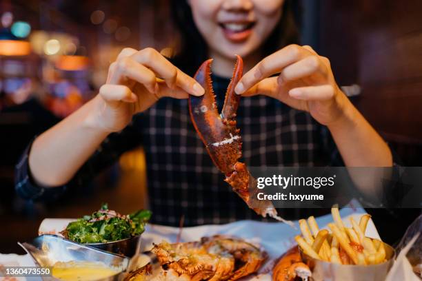 smiling asian woman holding a grilled lobster claw in restaurant - vis en zeevruchten stockfoto's en -beelden
