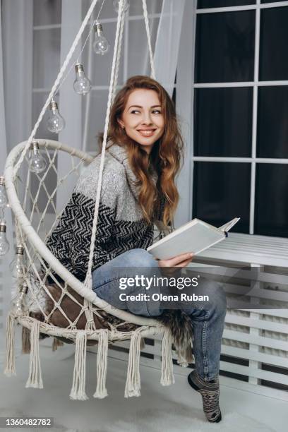 young woman reading book sitting in hanging chair. - live in levis event stock pictures, royalty-free photos & images