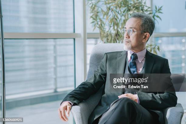 successful asian chinese senior manager looking away sitting at office lounge - alleen seniore mannen stockfoto's en -beelden
