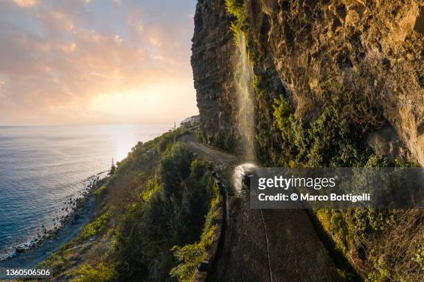 car passing under a waterfall on a road in madeira, portugal - cliff road stock pictures, royalty-free photos & images