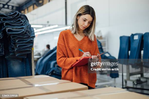 trabajadora tomando notas de la caja de ropa en la fábrica - fashion director fotografías e imágenes de stock