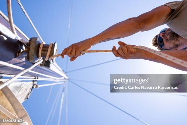 man pulling a rope to tie it up to the mast of a boat - albero maestro foto e immagini stock