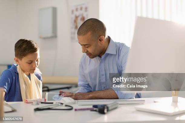 male pediatrician showing digital x-ray to boy with arm in sling - x ray arm stock pictures, royalty-free photos & images