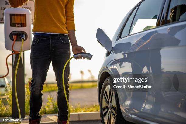 hombre afroamericano insertando enchufe en la toma de carga del coche eléctrico - parking meter fotografías e imágenes de stock