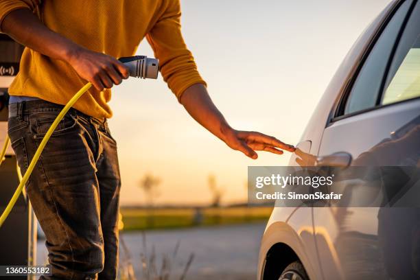 african american man inserting plug into the electric car charging socket - hybrid car stockfoto's en -beelden