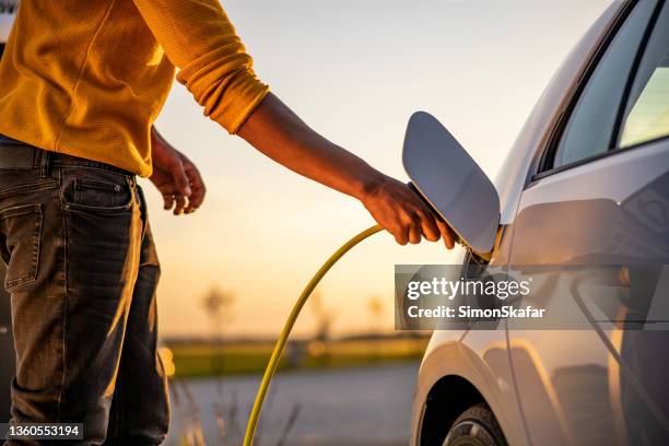 african american man inserting plug into the electric car charging socket - elektrische auto stockfoto's en -beelden