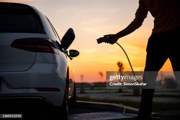 silhouette de l’homme insérant une prise dans la prise de recharge de la voiture électrique - insérer photos et images de collection