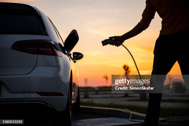 silhouette of man inserting plug into the electric car charging socket - tesla motors stock pictures, royalty-free photos & images
