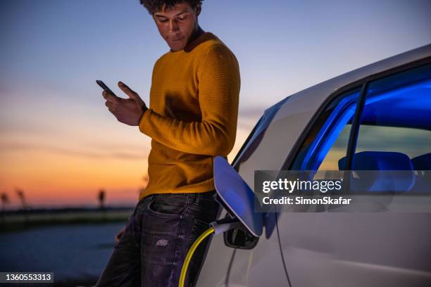 man using mobile phone while charging electric car - elektroauto tanken stockfoto's en -beelden