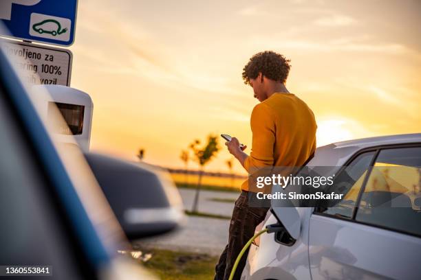 mann mit handy beim aufladen des elektroautos - fuel efficient stock-fotos und bilder