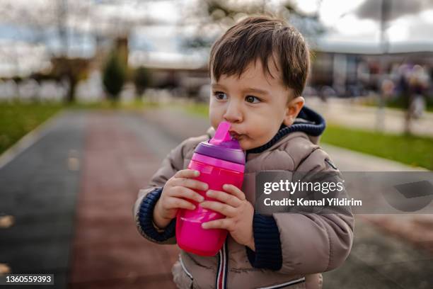 baby boy is drinking water bottle container while at the park - boy drinking water stock pictures, royalty-free photos & images