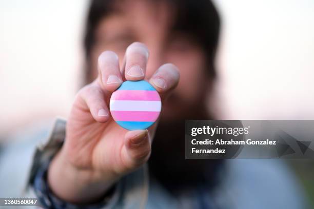 an unrecognizable bearded man holding and showing a pin with transgender colors flag - transgender symbol stock pictures, royalty-free photos & images