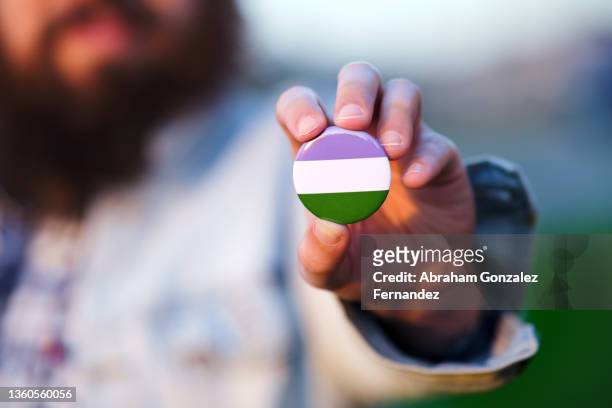 an unrecognizable bearded man holding and showing a pin with gender queer colors flag - denim jacket badges stock pictures, royalty-free photos & images