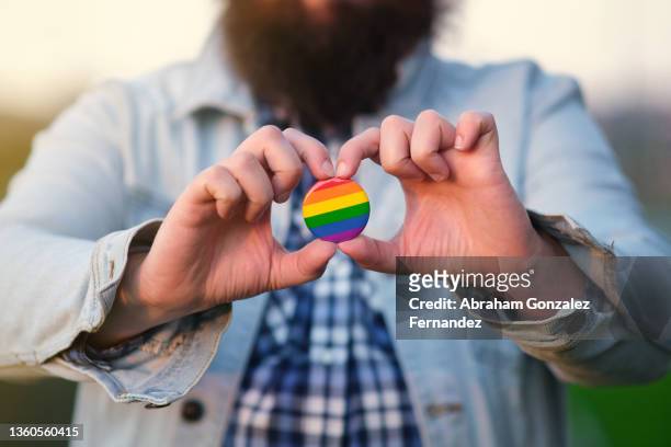 an unrecognizable bearded man holding and showing a pin with rainbow colors. - denim jacket badges stock pictures, royalty-free photos & images