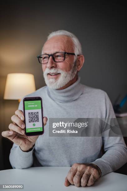 senior man showing vaccination certificate on the phone - tonen stockfoto's en -beelden