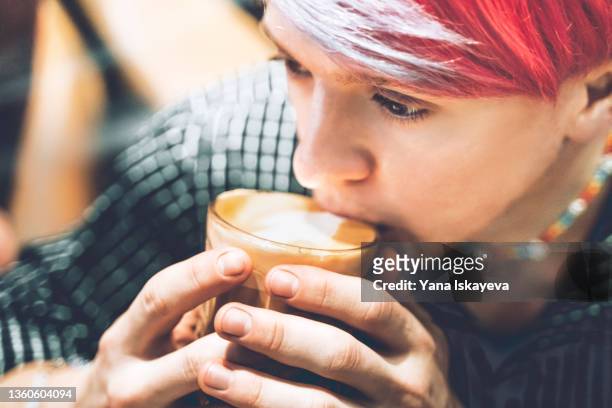 close-up portrait of a young informal man with colorful hair and accessories, drinking coffee at a cafe - purple hair stock-fotos und bilder
