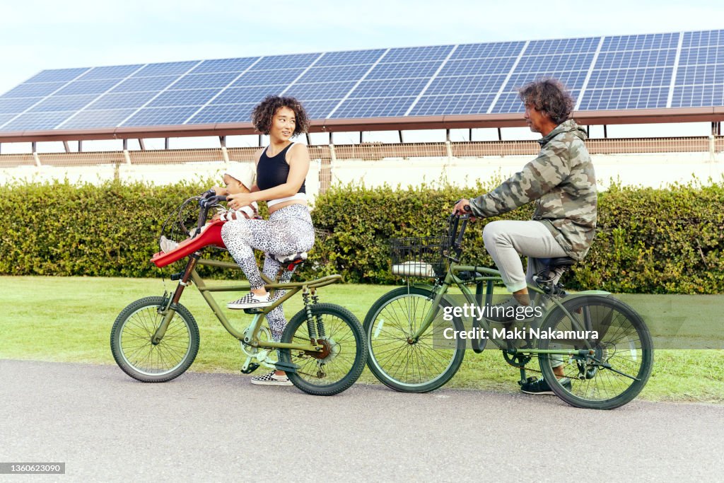 A two-year-old boy is being carried along on his mother's bicycle, riding along the road in front of the solar panels.