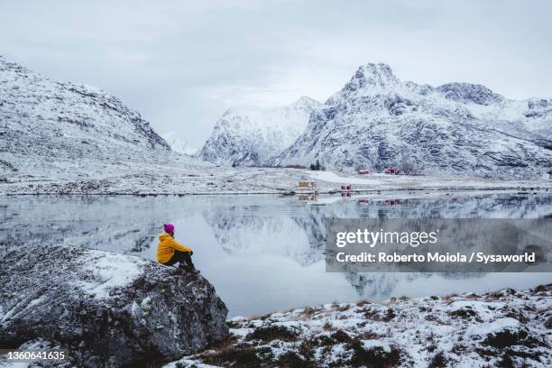 man admiring mountains from frozen fjord in winter, norway - schneebedeckt stock-fotos und bilder