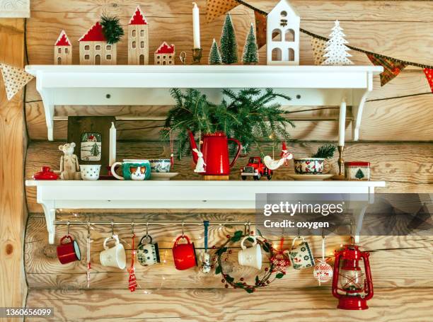 two white shelfs with christmas decorations on wooden log cabin background. interior kitchen green and red christmas decor. - continental_shelf stock pictures, royalty-free photos & images