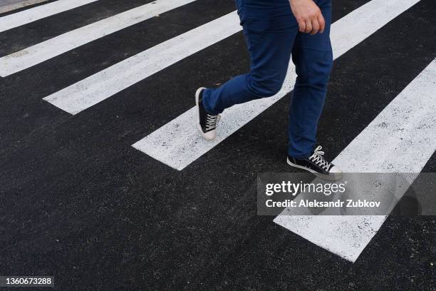 a young man walks alone on a pedestrian crossing. the legs of a guy in jeans and sneakers step on a white zebra stripe close-up. the concept of safety, proper lifestyle, compliance with traffic rules. - fußgänger stock-fotos und bilder