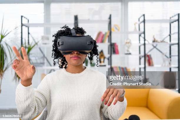travail virtuel. jeune femme africaine en casque vr pointant en l’air alors qu’elle est assise au bureau dans un bureau créatif - casques réalité virtuelle photos et images de collection