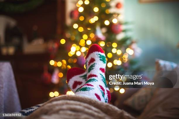 feet in christmas socks rest in the warmth of the home. in the background there are lights of a christmas tree - stocking feet fotografías e imágenes de stock