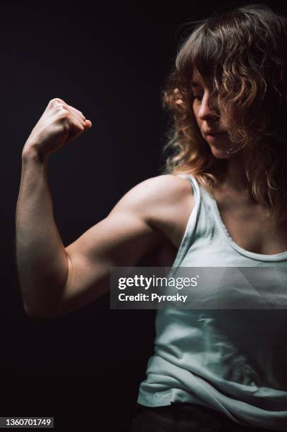 portrait of a young woman showing her arm and strength - bicep curl stockfoto's en -beelden