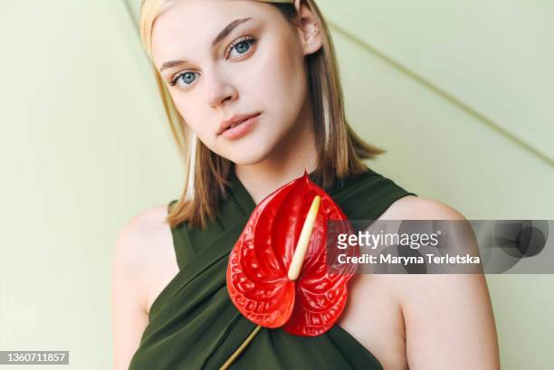 portrait of a girl in a green jumpsuit with an anthurium flower. light background. jumpsuit with an open back. girl with blond hair. green jumpsuit. sun shadows. red anthurium flower. - summer hair care stock pictures, royalty-free photos & images