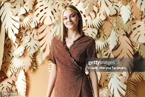 the girl in a brown dress on a tropical background of beige color. beige background. paper background. universal abstract background. brown wrap dress. girl with blond hair. - brown dress stock pictures, royalty-free photos & images