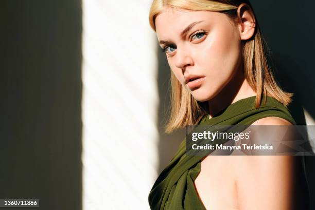 portrait of a girl in a green jumpsuit against the backdrop of sunbeams. light background. dark background. jumpsuit with an open back. girl with blond hair. green jumpsuit. sun shadows. - calções imagens e fotografias de stock