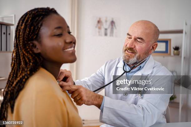 experienced doctor examining black female patient with stethoscope - listening skills stock pictures, royalty-free photos & images