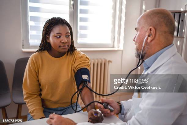 beautiful black woman has her blood pressure checked - hypertensive stock pictures, royalty-free photos & images