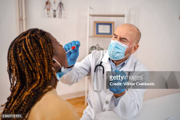 doctor testing black female patient on possible coronavirus infection by taking a swab from mouth - cotton bud stock pictures, royalty-free photos & images