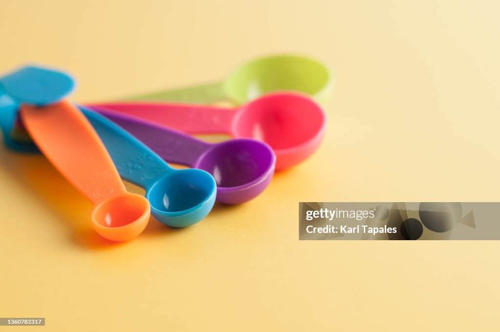 Financial concepts still life close-up of variety of vibrant colored measuring spoons on a yellow background
