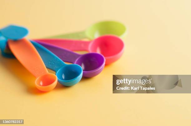 financial concepts still life close-up of variety of vibrant colored measuring spoons on a yellow background - measuring spoon stock pictures, royalty-free photos & images