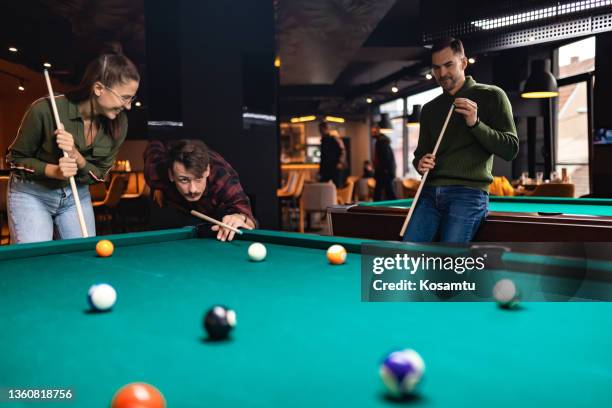ein junger mann legt kreide auf seinen billardstock, während seine freunde an der reihe sind, die billardkugeln zu schlagen. - queue stock-fotos und bilder