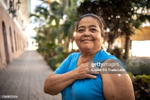 portrait of a senior woman vaccinated showing her arm with a bandage outdoors - true peoples celebration day one stock pictures, royalty-free photos & images