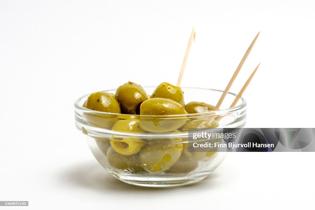 Green olives in a clear bowl. Isolated against a white background