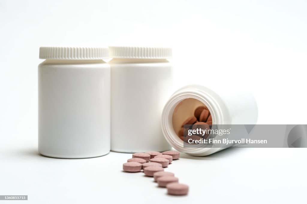 Three neutral white pill boxes. One lying open with pills on the outside Isolated against white background. Neutral pink pills in front of the boxes