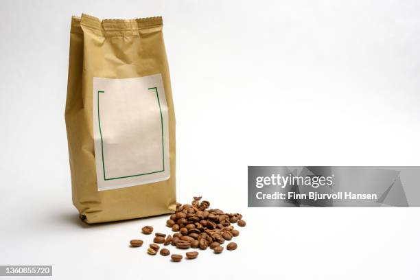 gray coffee bag. decorated with label. coffee beans in front of the bag. isolated against white background - coffee bag stock-fotos und bilder