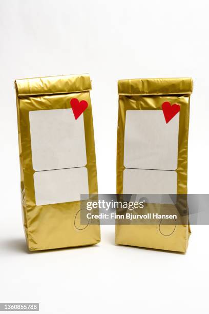 two gold-colored coffee bags. decorated with red heart and label. isolated against white background - finn bjurvoll imagens e fotografias de stock